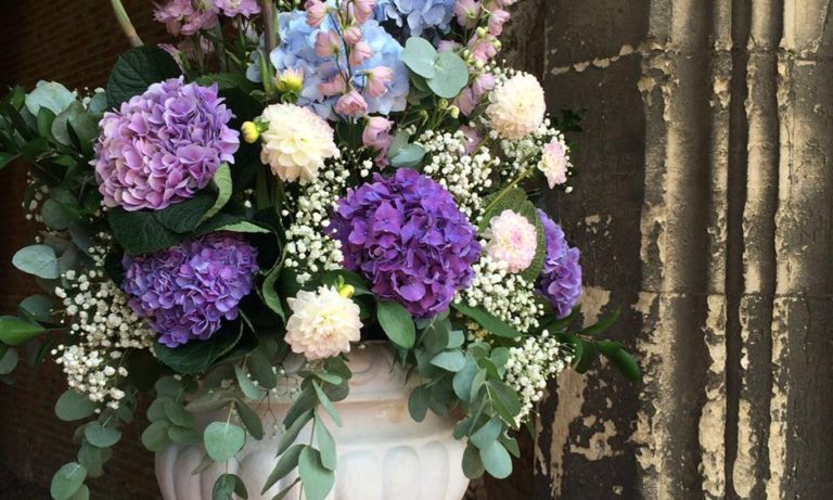 Blue and purple hydrangeas, delphinium, gypsophila and eucalyptus displayed in a white urn