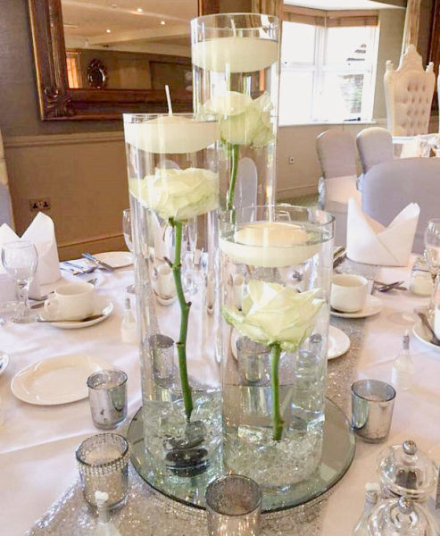 Three different height cylindrical vases each containing a single submerged rose and floating candle
