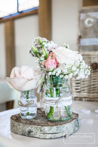 Jars of flowers with lace ribbon displayed on a log slice