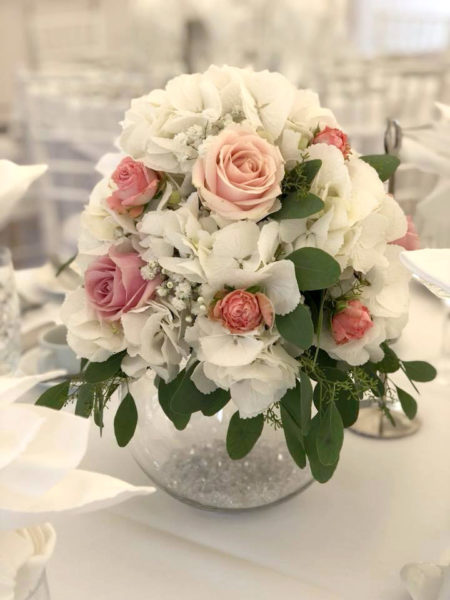 Cream and pink flower arrangement placed on top of a fish bowl vase