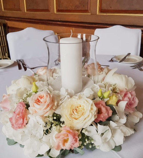 Glass hurricane vase with large candle surrounded by a ring of flowers