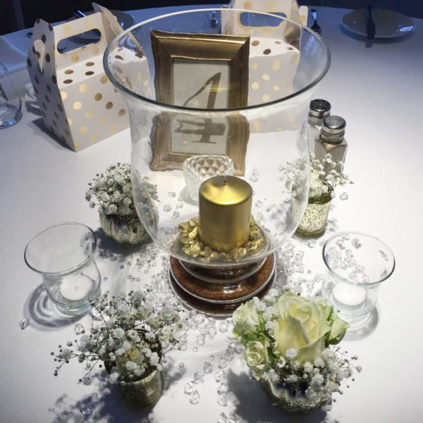 Wedding centrepiece with Hurricane Lamp and gold candle surrounded by small vases of flowers