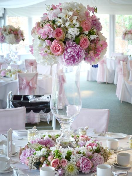 Tall glass vase with a pink and white flower arrangement on top and ring of flowers around the base
